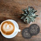 Two engraved highland cow sunflower slate coasters beside a latte and a succulent on a wood table (product mockup)