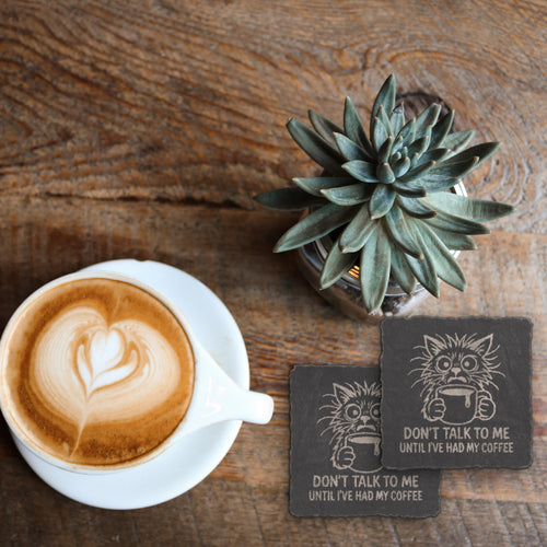 Engraved coffee cat slate coaster under a latte beside a succulent on a wood table (product mockup)