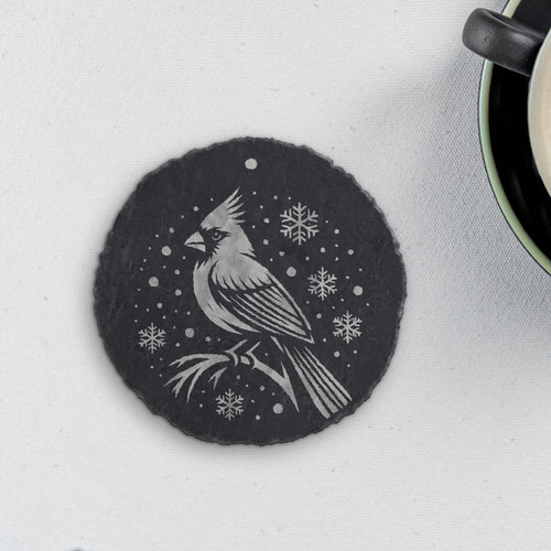 Round slate coaster engraved with a cardinal on a branch among snowflakes (product mockup)