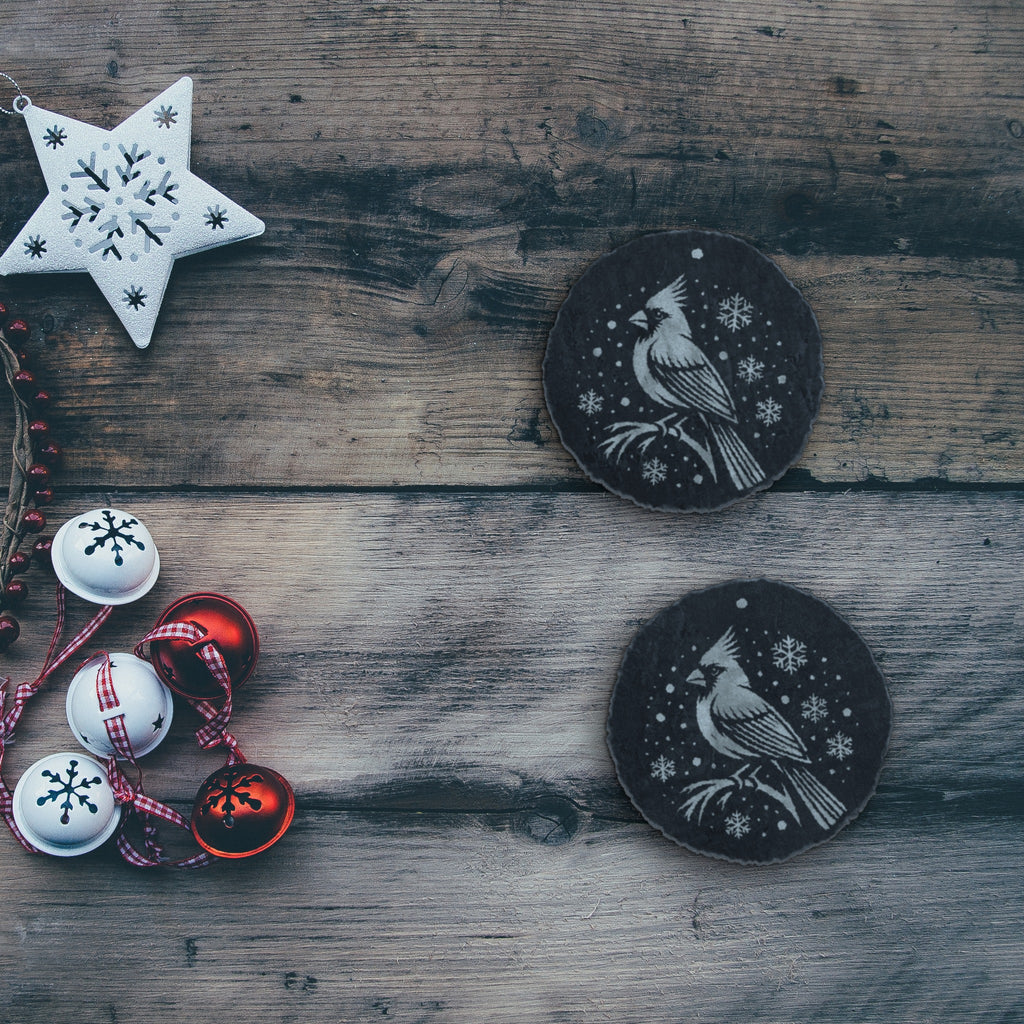 Two cardinal slate coasters on a rustic wood table with holiday decorations (product mockup)