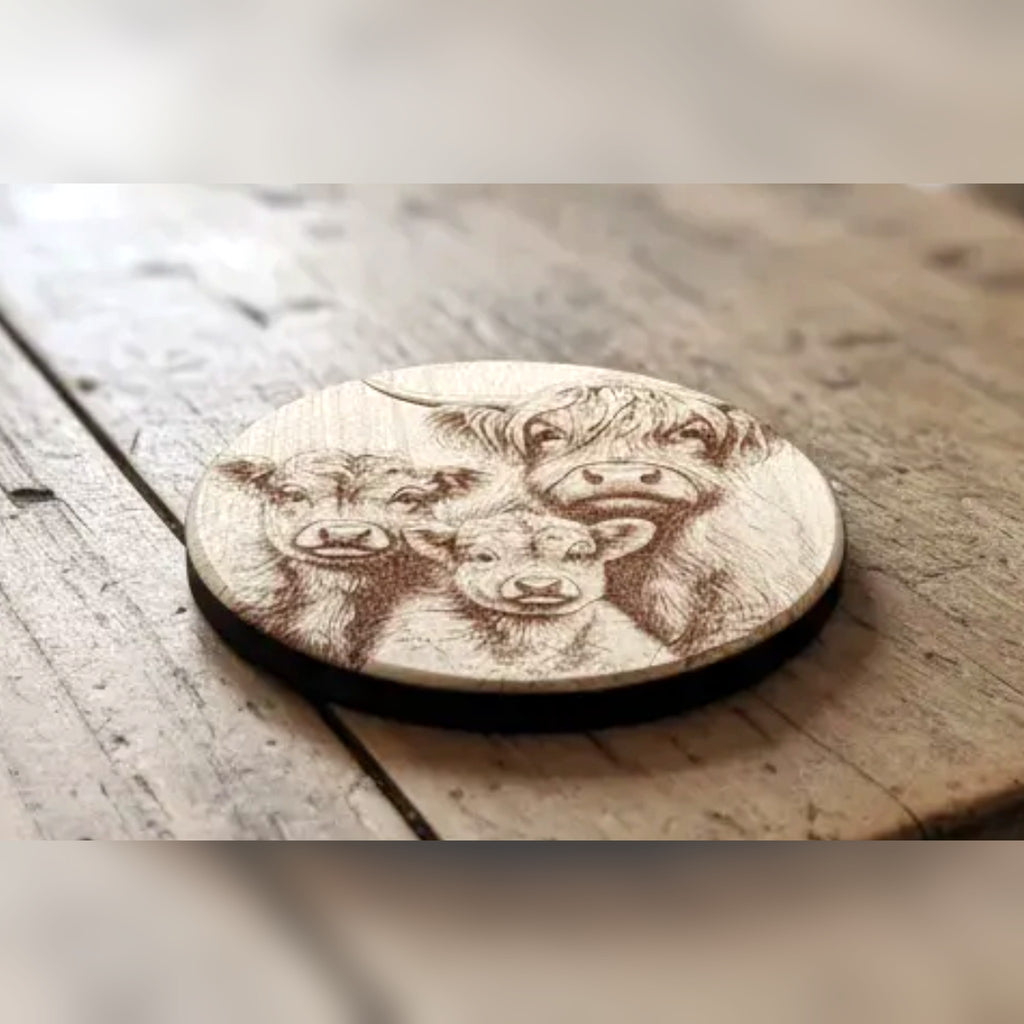 Highland cow family design engraved on the designer's round wood sample coaster on a rustic table