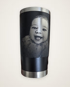 Black tumbler laser engraved with a smiling baby's photo, held in a hand (real photo of our work)