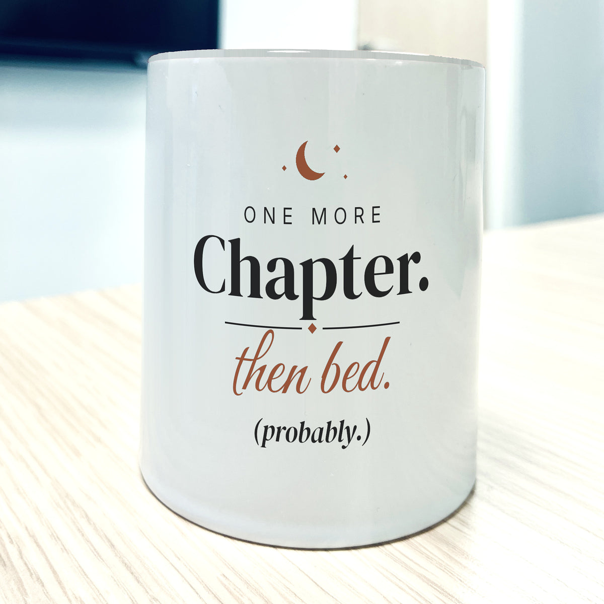 White 11oz mug, front view, printed "One more Chapter. then bed. (probably.)" in charcoal and terracotta with a small crescent moon.