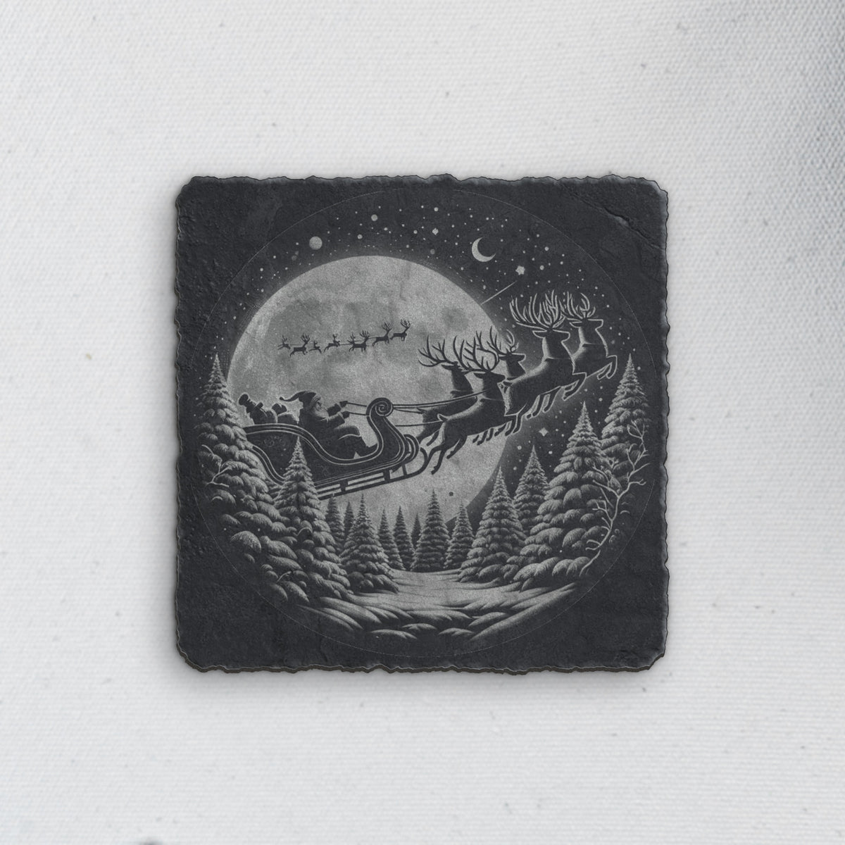 Square slate coaster engraved with Santa's sleigh flying past the moon over snowy pines (product mockup)