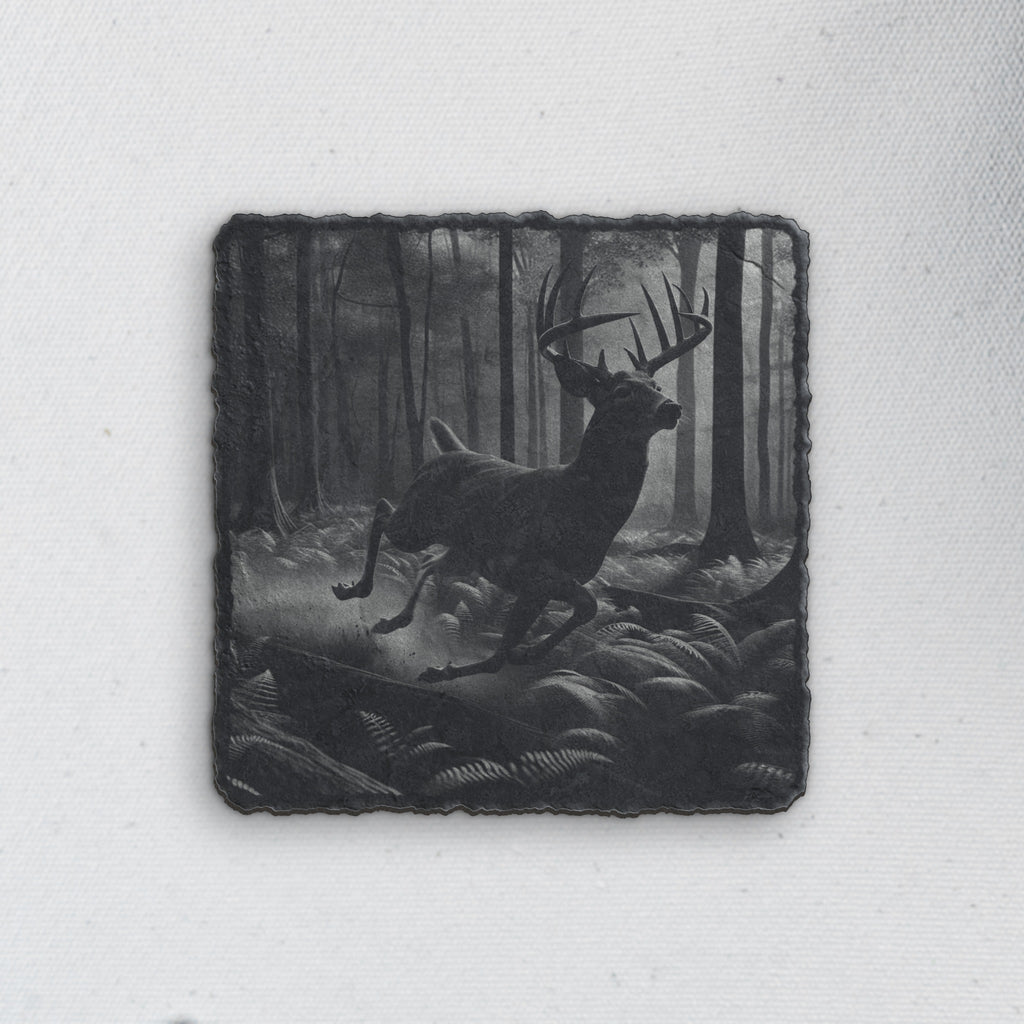 Square slate coaster engraved with a whitetail buck leaping through a misty forest (product mockup)