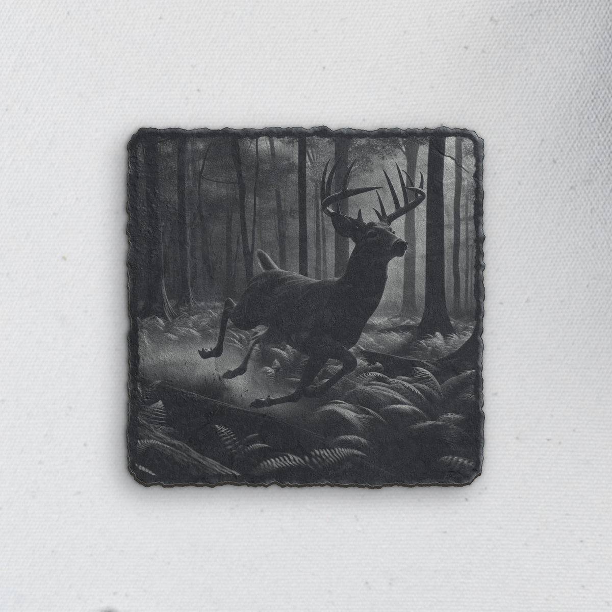 Square slate coaster engraved with a whitetail buck leaping through a misty forest (product mockup)