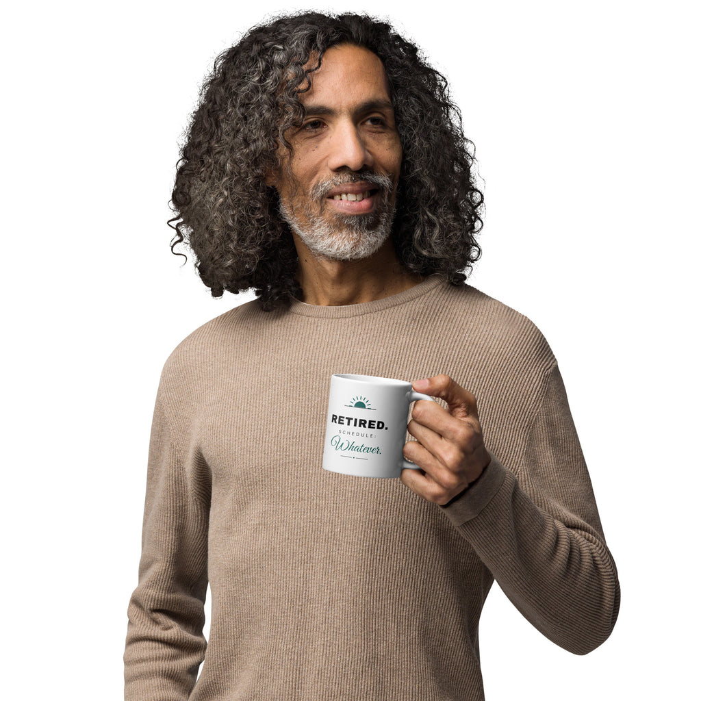 White glossy 11oz mug, handle on the right, printed "RETIRED. Schedule: Whatever." in charcoal and teal script under a small rising-sun mark.